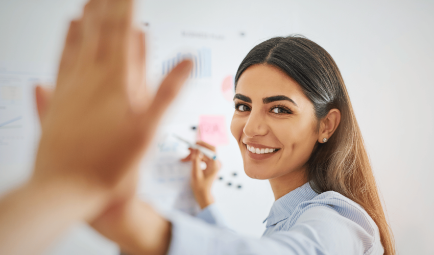 professional woman high-fiving coworker happily while writing on white board