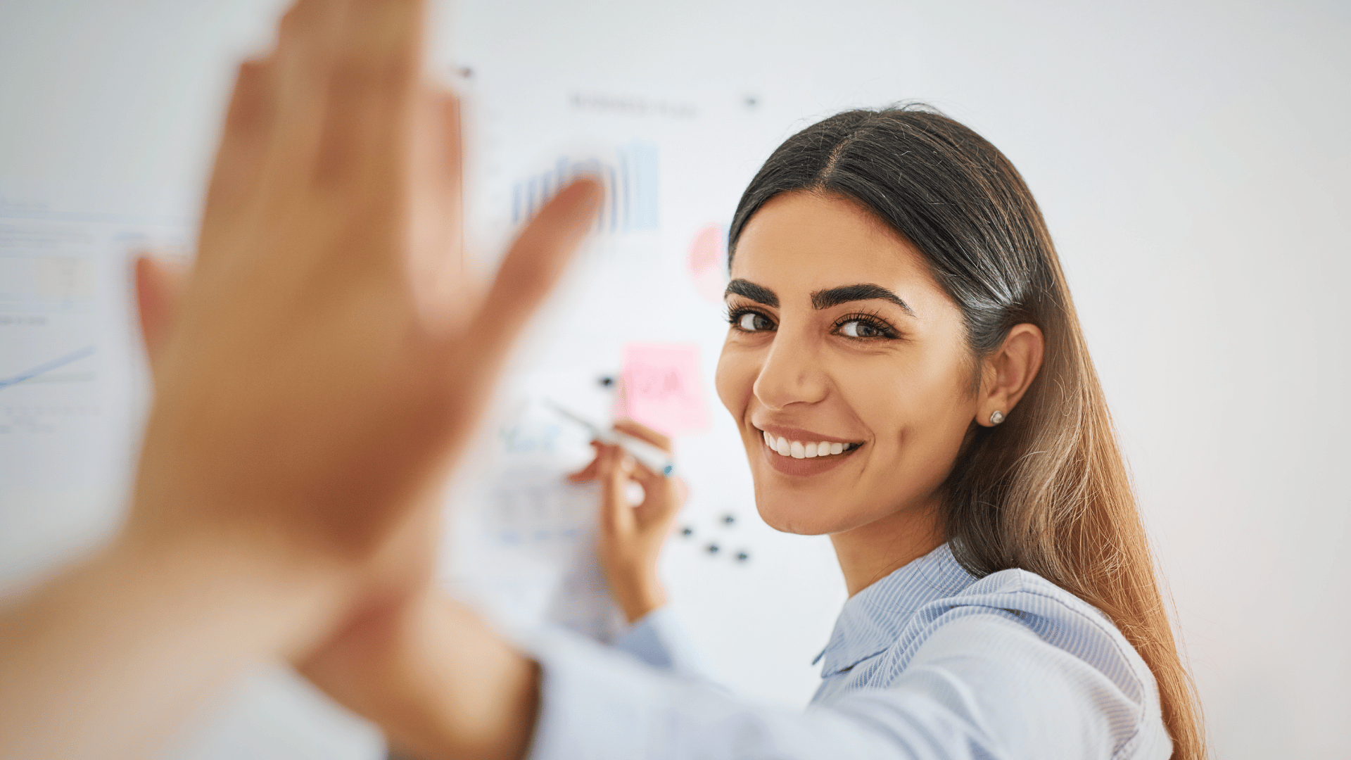 professional woman high-fiving coworker happily while writing on white board